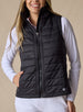 Cloud Vest in Black, front view on model featuring a black quilted full-zip vest with mock neck collar and front pockets with hand inserted styled with a white long sleeve top and white pants