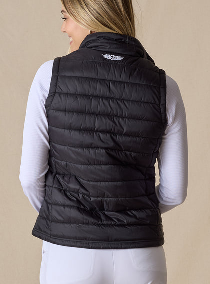 Cloud Vest in Black, back view on model featuring a black quilted vest with Straight Down embroidered logo at the center back neck styled with a white long sleeve top and white pants