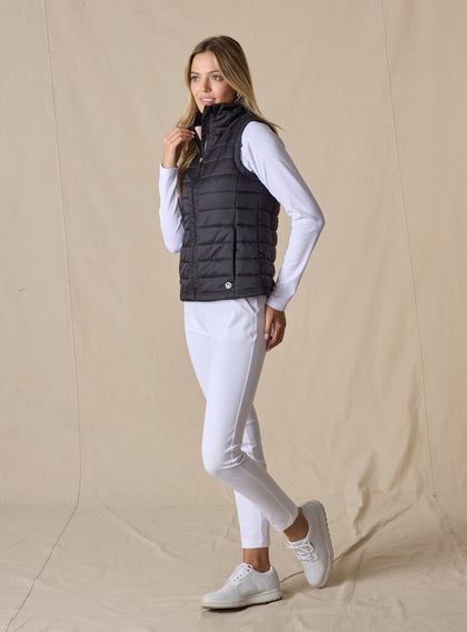 Cloud Vest in Black, side view on model featuring a black quilted full-zip vest with mock neck collar and Straight Down logo at the hem styled with a white long sleeve top, white pants, and white shoes