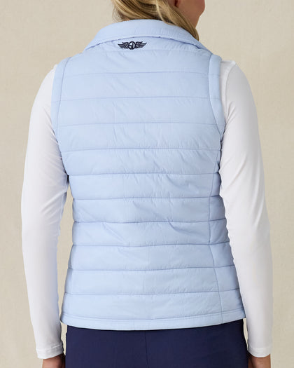 Cloud Vest in Powder, back view on model featuring a light blue quilted vest with navy embroidered logo detail at the center back neck styled with a white long sleeve top and navy pants