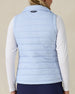 Cloud Vest in Powder, back view on model featuring a light blue quilted vest with navy embroidered logo detail at the center back neck styled with a white long sleeve top and navy pants