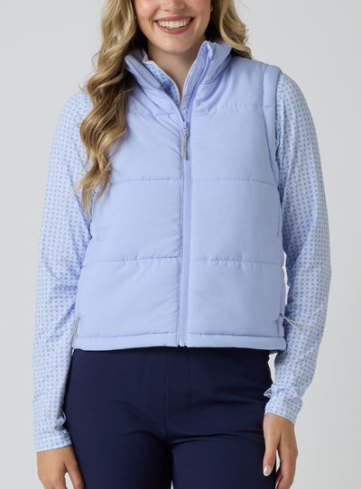 Women's Sandy Vest in Lavender, front view on model featuring a light purple quilted puffer vest layered over a patterned long sleeve top, paired with navy pants