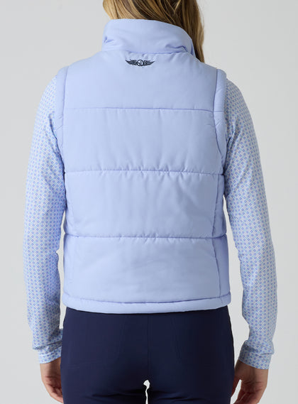 Women's Sandy Vest in Lavender, back view on model featuring the Straight Down logo embroidered at center back on a light purple quilted puffer vest, layered over a patterned long sleeve top, paired with navy pants