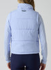 Women's Sandy Vest in Lavender, back view on model featuring the Straight Down logo embroidered at center back on a light purple quilted puffer vest, layered over a patterned long sleeve top, paired with navy pants