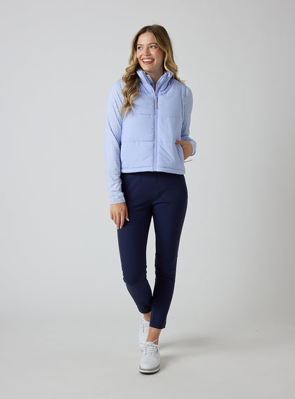 Women's Sandy Vest in Lavender, full length front view on model featuring a light purple quilted puffer vest layered over a patterned long sleeve top, paired with navy pants and white golf shoes