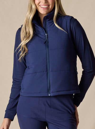 Women's Sandy Vest in New Indigo, front view on model featuring a navy quilted puffer vest layered over a navy long sleeve top, paired with navy pants