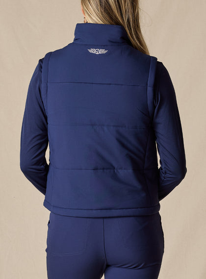 Women's Sandy Vest in New Indigo, back view on model featuring the Straight Down logo embroidered at center back on a navy quilted puffer vest, layered over a navy long sleeve top, paired with navy pants