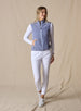 Lucia Vest in Bluestone, full length front view on model featuring a blue-violet fleece full-zip vest with mock neck collar and light blue contrast zipper styled with a white long sleeve top, white pants, and white shoes