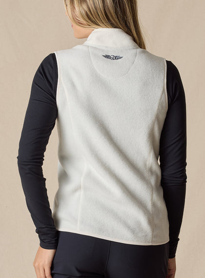Lucia Vest in Cream, back view on model featuring an ivory fleece vest with embroidered logo detail at the center back neck styled with a black long sleeve top and black pants