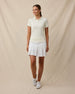 Woman wearing the Sindy Rib Knit Polo in Coconut with a white pleated golf skort and white golf shoes.