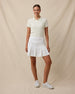 Woman wearing the Sindy Rib Knit Polo in Coconut tucked into a white pleated golf skort with white golf shoes.