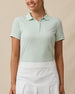 Front view of a woman wearing the Sindy Polo in Lemongrass with a white skort, highlighting the ribbed fabric and contrast trim.