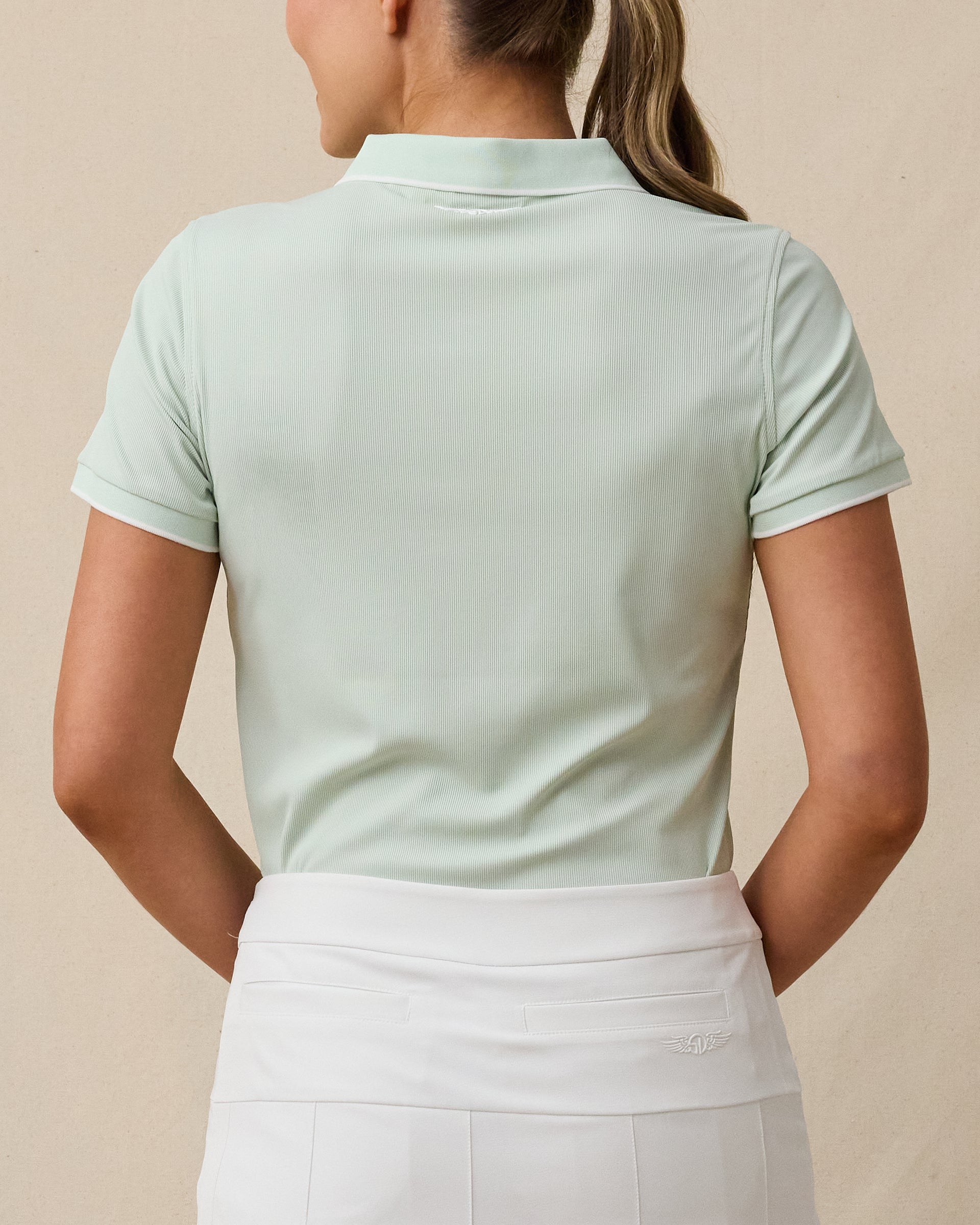 Back view of a woman wearing the Sindy Polo in Lemongrass with a white skort.