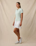 Full-length side view of a woman wearing the Sindy Polo in Lemongrass with a white pleated skort and white golf shoes.