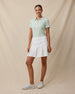 Full-length front view of a woman wearing the Sindy Polo in Lemongrass with a white pleated skort and white golf shoes.