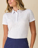 Women's Cherry Bloom Polo in White, front view on model featuring an allover purple and pink scattered floral print, paired with navy pants