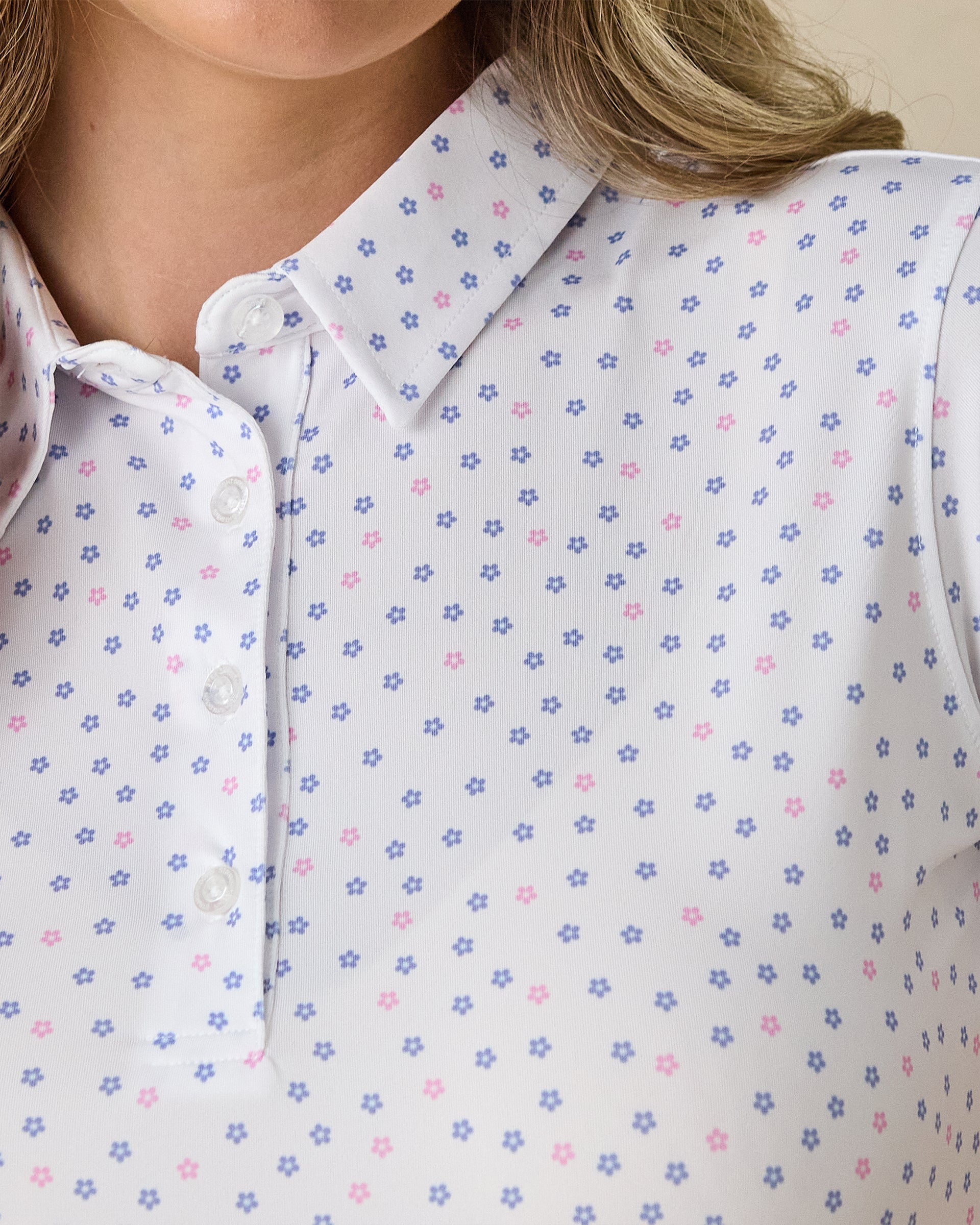 Women's Cherry Bloom Polo in White, close-up front view on model highlighting the purple and pink scattered floral print and white button placket detail