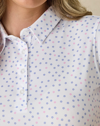 Women's Cherry Bloom Polo in White, close-up front view on model highlighting the purple and pink scattered floral print and white button placket detail