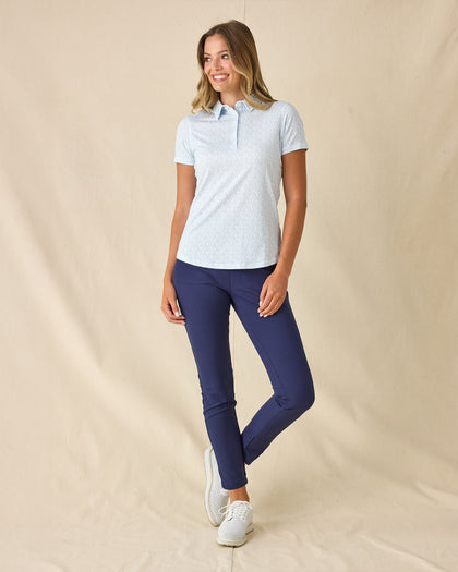 Dog Mom Polo in Coastal, full length front view worn by a model paired with navy ankle pants and white golf shoes, showcasing the light blue and white allover dog print pattern