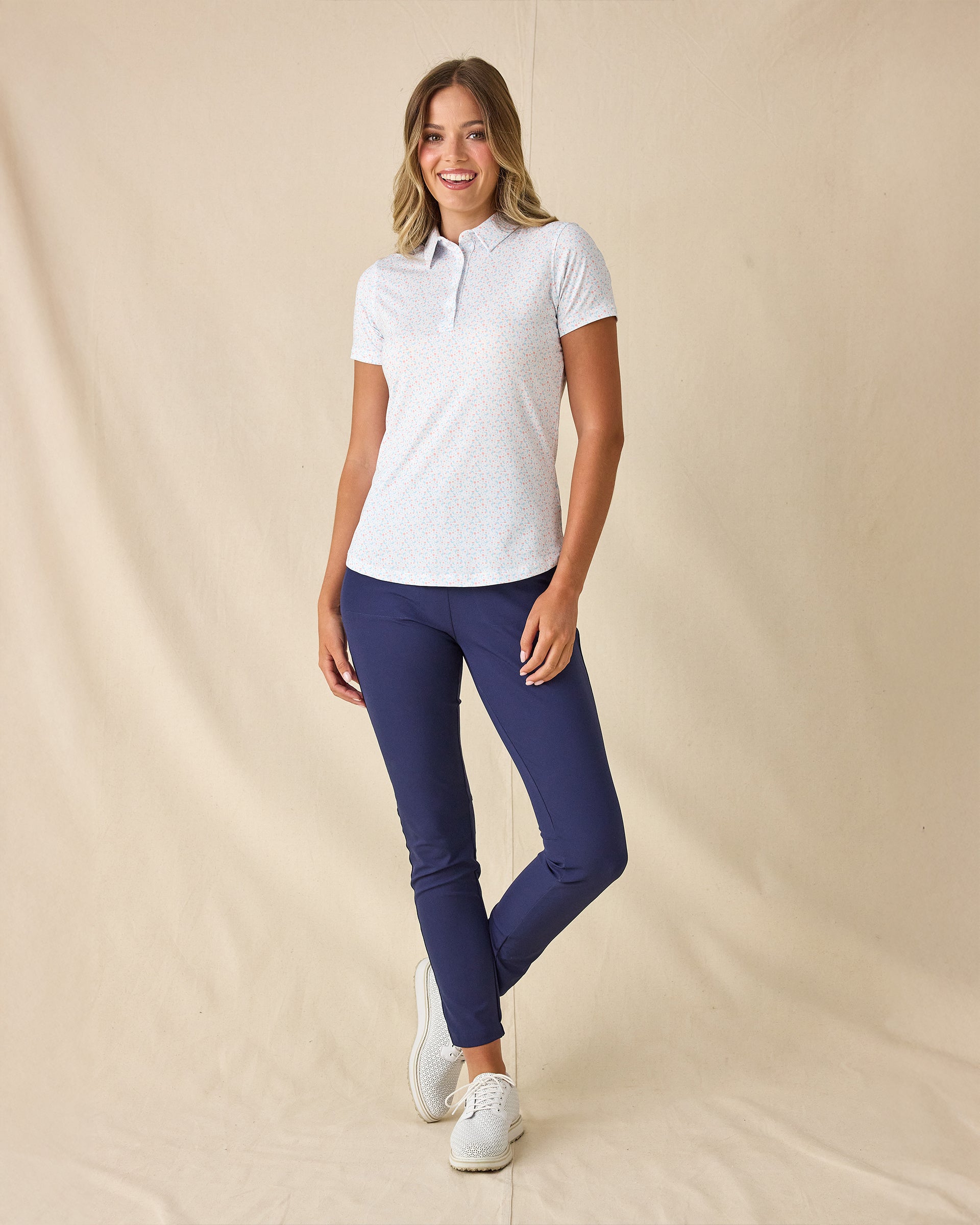 Spring Valley Polo in Spritz, full length front view featuring a white base with light blue floral vine and coral dot allover print pattern, paired with navy ankle pants and white golf shoes