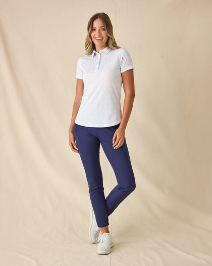 Spring Valley Polo in Spritz, full length front view featuring a white base with light blue floral vine and coral dot allover print pattern, paired with navy ankle pants and white golf shoes