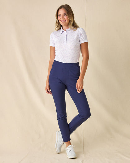 Women's Kokomo Polo in White, full length front view on model featuring an allover purple sketch-style tropical print with palm trees, florals, turtles, dolphins and pelicans, paired with navy pants and white shoes