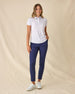 Women's Kokomo Polo in White, full length front view on model featuring an allover purple sketch-style tropical print with palm trees, florals, turtles, dolphins and pelicans, paired with navy pants and white shoes