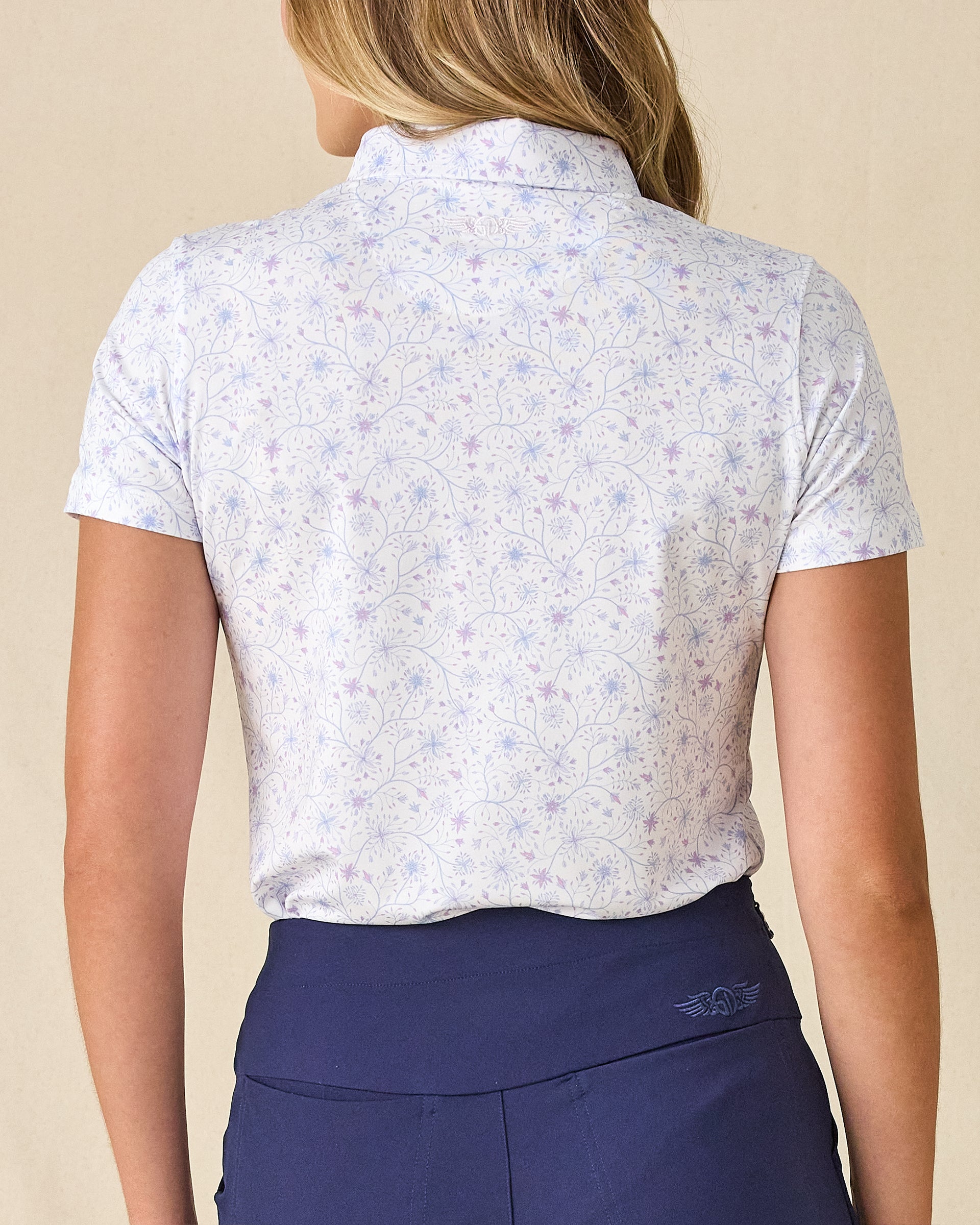 Women's Mariette Polo in Pink Floyd, back view on model featuring an allover blue and purple vine floral print with tonal Straight Down logo embroidered at center back neck, paired with navy pants