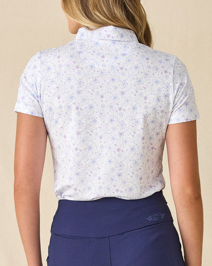 Women's Mariette Polo in Pink Floyd, back view on model featuring an allover blue and purple vine floral print with tonal Straight Down logo embroidered at center back neck, paired with navy pants