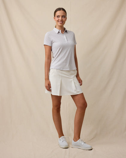 Full-length view of a woman wearing the Martini Girl Polo in Lemongrass with a white pleated skort and white golf shoes.