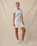 Full-length view of a woman wearing the Martini Girl Polo in Lemongrass with a white pleated skort and white golf shoes.