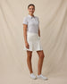 Full-length three-quarter view of a woman wearing the Martini Girl Polo in Lemongrass paired with a white pleated skort and white golf shoes.