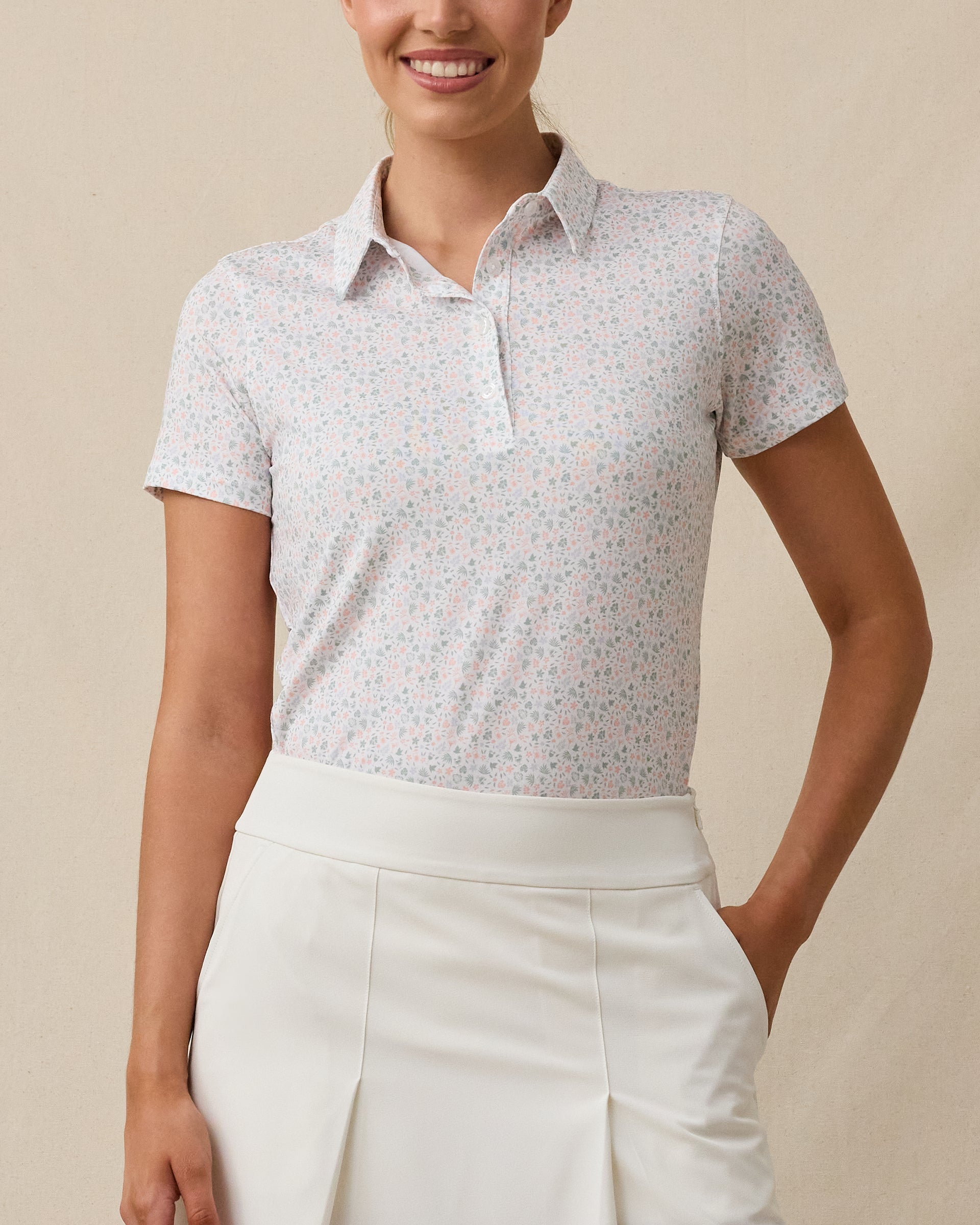 Front view of a woman wearing the Palm Island Polo in Lemongrass with a white skort, showing the allover tropical print and button placket.