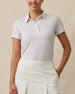 Front view of a woman wearing the Palm Island Polo in Lemongrass with a white skort, showing the allover tropical print and button placket.