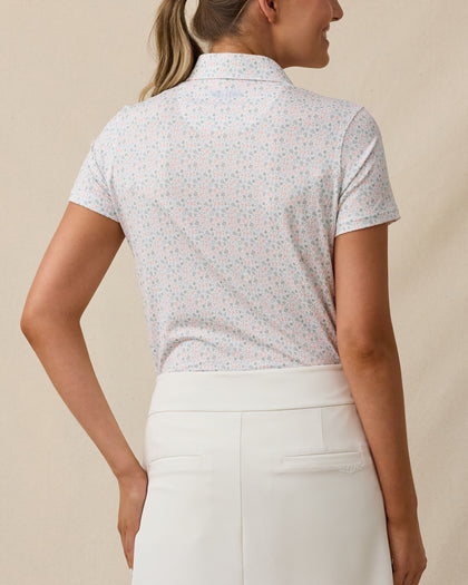 Back view of a woman wearing the Palm Island Polo in Lemongrass, showing the allover tropical print and embroidered logo below the back collar.