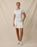 Full-length front view of a woman wearing the Palm Island Polo in Lemongrass with a white pleated skort and white golf shoes.