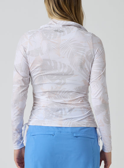 Straight Down Women's Flora Quarter Zip in White, back view on model featuring a white long sleeve quarter zip pullover with an allover neutral tropical leaf print and side ruching detail, paired with a blue skort