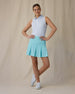 Women's Juno Stripe Sleeveless Polo in Glacier, full-length front on-model view with hands on hips featuring a white sleeveless polo with a blue and mint multi-stripe pattern, spread collar, and two-button placket, paired with a mint green pleated skirt and white shoes
