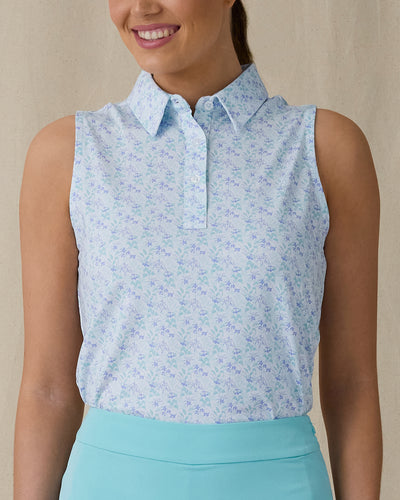 Women's Costa Rica Sleeveless Polo in Green Stone, front on-model view from the waist up featuring a white sleeveless polo with an allover small floral and leaf print in blue and mint green tones, spread collar, and three-button placket, paired with a mint green skirt