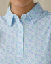 Women's Costa Rica Sleeveless Polo in Green Stone, close-up front on-model view highlighting the spread collar and three-button placket detail featuring an allover small floral and leaf print in blue and mint green tones on a white base