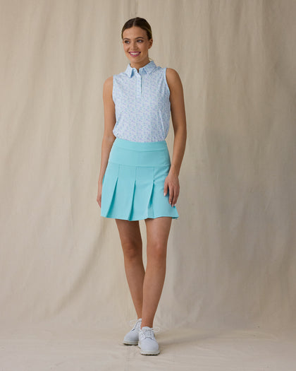 Women's Costa Rica Sleeveless Polo in Green Stone, full-length front on-model view with a relaxed stance featuring a white sleeveless polo with an allover small floral and leaf print in blue and mint green tones, spread collar, and three-button placket, paired with a mint green pleated skirt and white shoes