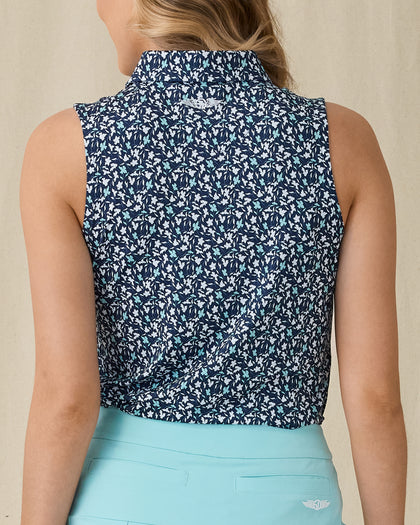 Women's Flores Sleeveless Polo in New Indigo, back on-model view featuring a navy sleeveless polo with an allover small floral print in white and mint green tones, spread collar, and Straight Down logo embroidered at the upper back, paired with a mint green skirt