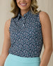 Women's Flores Sleeveless Polo in New Indigo, front on-model view from the waist up featuring a navy sleeveless polo with an allover small floral print in white and mint green tones, spread collar, and two-button placket, paired with a mint green skirt