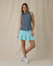 Women's Flores Sleeveless Polo in New Indigo, full-length front on-model view featuring a navy sleeveless polo with an allover small floral print in white and mint green tones, spread collar, and two-button placket, paired with a mint green pleated skirt and white shoes