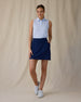 Women's Hydra Sleeveless Polo in Lavender, full-length front on-model view with a relaxed stance featuring a white sleeveless polo with an allover small floral print in light blue tones, spread collar, and two-button placket, paired with a navy skort and white shoes