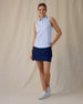Women's Hydra Sleeveless Polo in Lavender, full-length front on-model view with hand on hip featuring a white sleeveless polo with an allover small floral print in light blue tones, spread collar, and two-button placket, paired with a navy skort and white shoes