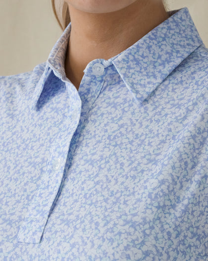 Women's Hydra Sleeveless Polo in Lavender, close-up front on-model view highlighting the spread collar and two-button placket detail featuring an allover small floral print in light blue tones on a white base