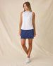 Valerie Sleeveless Polo in Spritz, full length front angle view featuring a white base with coral floral and light blue vine allover print pattern, paired with a navy skort and white golf shoes