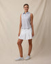 Full-length view of a woman wearing the Milano Sleeveless Polo in Lake paired with a white pleated skort and white golf shoes.