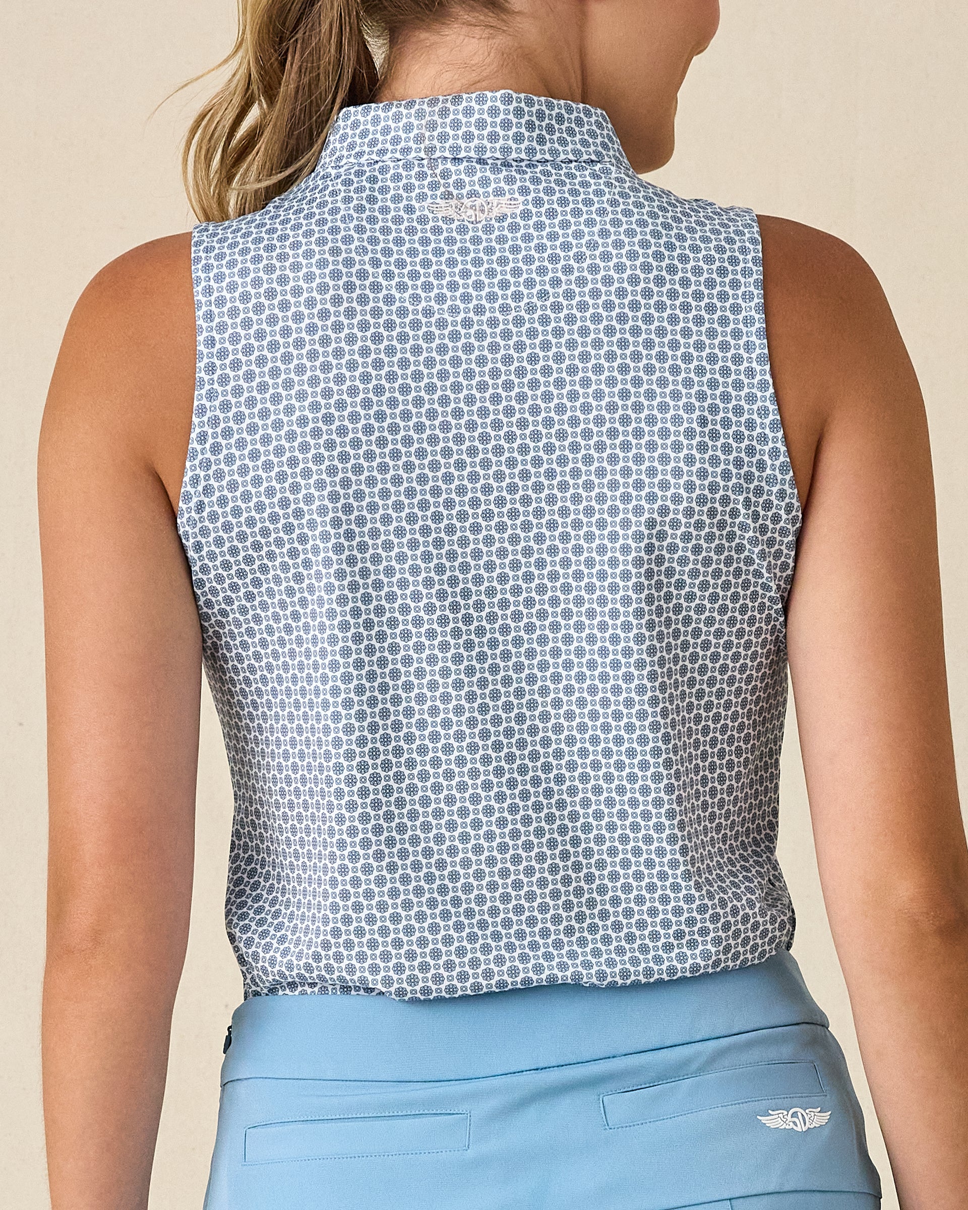 Milano Sleeveless Polo in Gemstone, back view featuring a white base with navy geometric medallion allover print pattern with Straight Down embroidered logo at the back collar, paired with a light blue skort